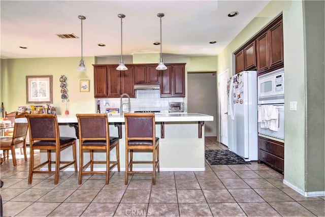 kitchen with pendant lighting, white appliances, tile patterned flooring, tasteful backsplash, and a kitchen island with sink