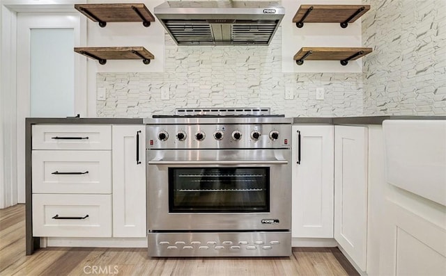 kitchen with white cabinets, high end range, extractor fan, decorative backsplash, and light wood-type flooring