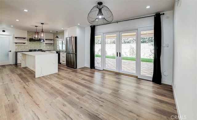 kitchen featuring backsplash, a kitchen island, white cabinetry, hanging light fixtures, and stainless steel fridge