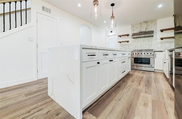 kitchen featuring decorative light fixtures, white cabinetry, tasteful backsplash, stainless steel stove, and light hardwood / wood-style flooring