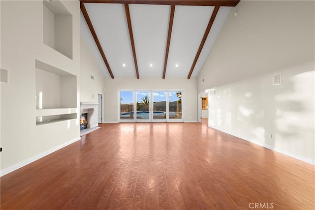 unfurnished living room featuring beamed ceiling, a towering ceiling, and hardwood / wood-style floors