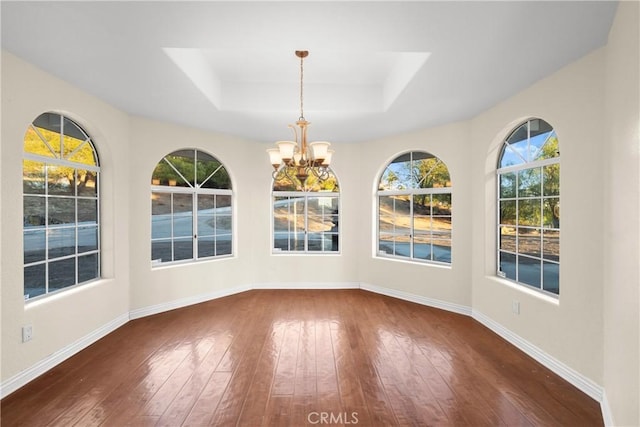 unfurnished dining area with a raised ceiling, dark hardwood / wood-style flooring, and a chandelier