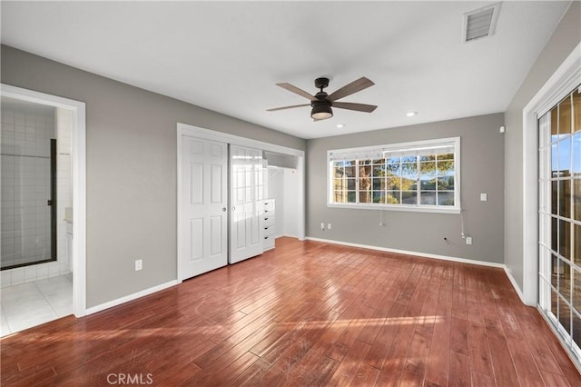 unfurnished bedroom featuring hardwood / wood-style flooring, ceiling fan, connected bathroom, and multiple windows