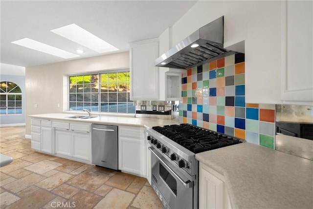 kitchen with sink, appliances with stainless steel finishes, white cabinetry, decorative backsplash, and wall chimney exhaust hood