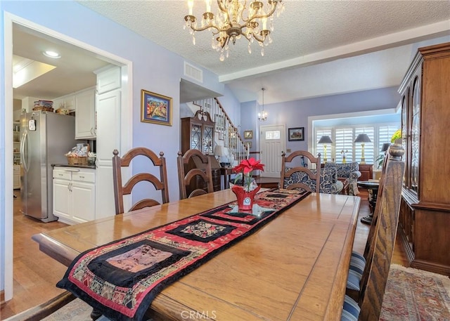 dining space with beamed ceiling, a textured ceiling, light hardwood / wood-style flooring, and a notable chandelier