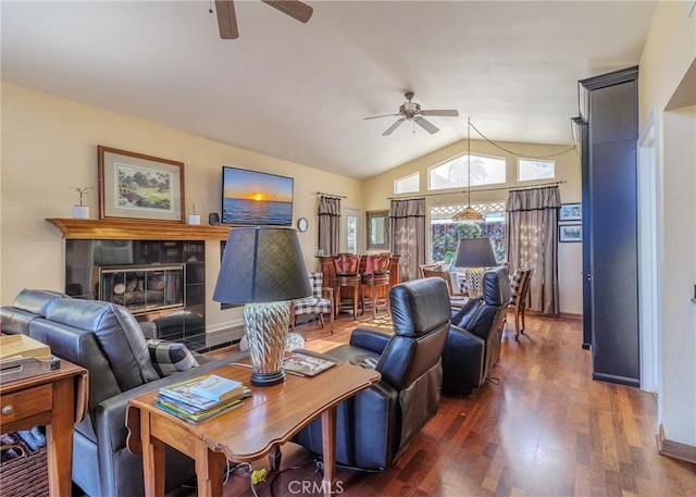 living room with ceiling fan, vaulted ceiling, dark wood-type flooring, and a tiled fireplace