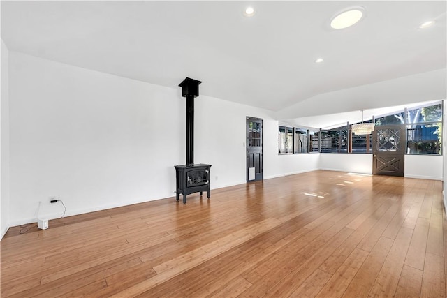 unfurnished living room featuring vaulted ceiling, light hardwood / wood-style floors, and a wood stove