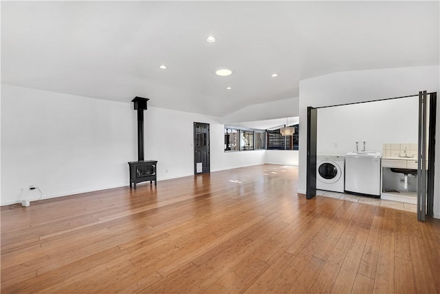 unfurnished living room featuring lofted ceiling, light hardwood / wood-style floors, a wood stove, sink, and independent washer and dryer