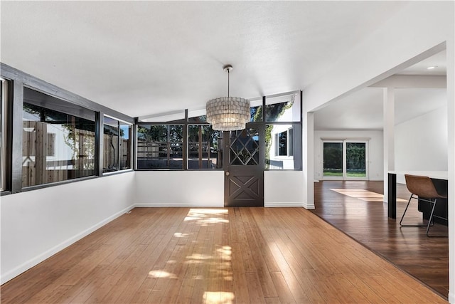 unfurnished dining area featuring wood-type flooring, vaulted ceiling, and a notable chandelier