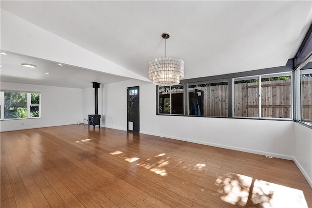 interior space featuring a notable chandelier, a wood stove, wood-type flooring, and lofted ceiling