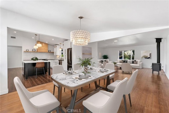 dining room featuring hardwood / wood-style floors, sink, a wood stove, an inviting chandelier, and vaulted ceiling