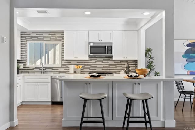 kitchen featuring hardwood / wood-style floors, sink, appliances with stainless steel finishes, a kitchen breakfast bar, and white cabinets