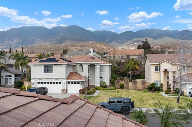 view of front facade with a garage, a mountain view, a front yard, and solar panels