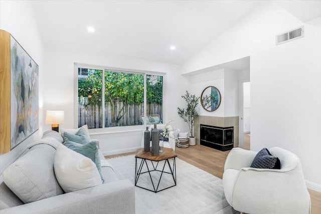 living room featuring a tile fireplace, vaulted ceiling, and light hardwood / wood-style flooring