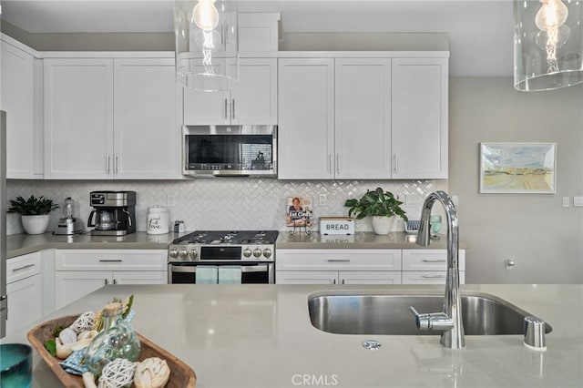 kitchen with appliances with stainless steel finishes, decorative light fixtures, white cabinetry, sink, and backsplash