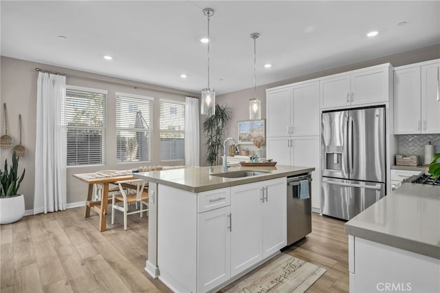 kitchen featuring an island with sink, stainless steel appliances, decorative light fixtures, white cabinets, and sink