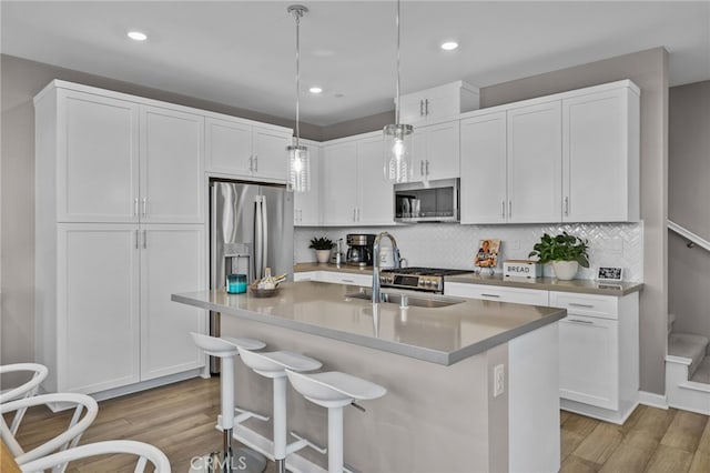 kitchen with white cabinetry, a center island with sink, stainless steel appliances, and hanging light fixtures