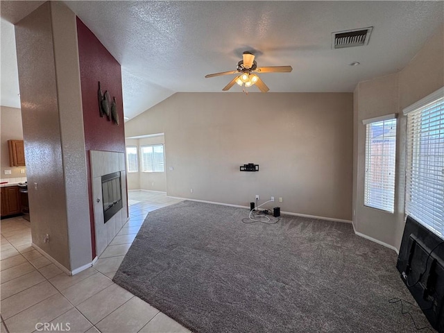 unfurnished living room featuring light tile patterned floors, ceiling fan, lofted ceiling, a fireplace, and a textured ceiling