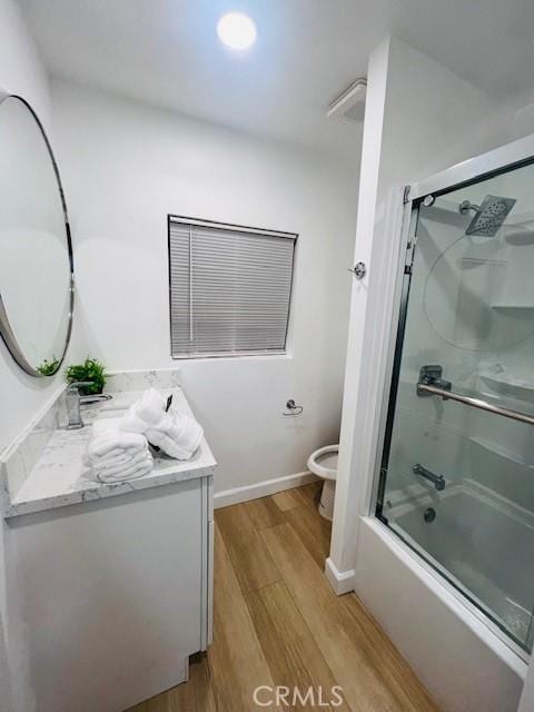 full bathroom featuring vanity, hardwood / wood-style floors, bath / shower combo with glass door, and toilet