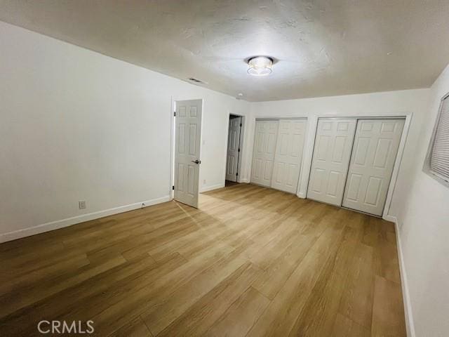 unfurnished bedroom with multiple closets and light hardwood / wood-style floors