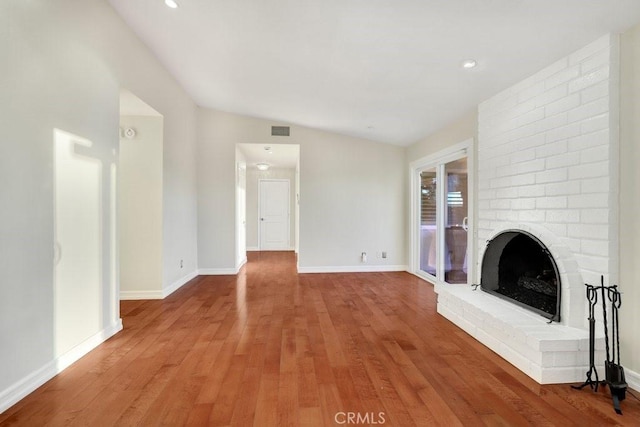 unfurnished living room with a brick fireplace, lofted ceiling, and hardwood / wood-style flooring