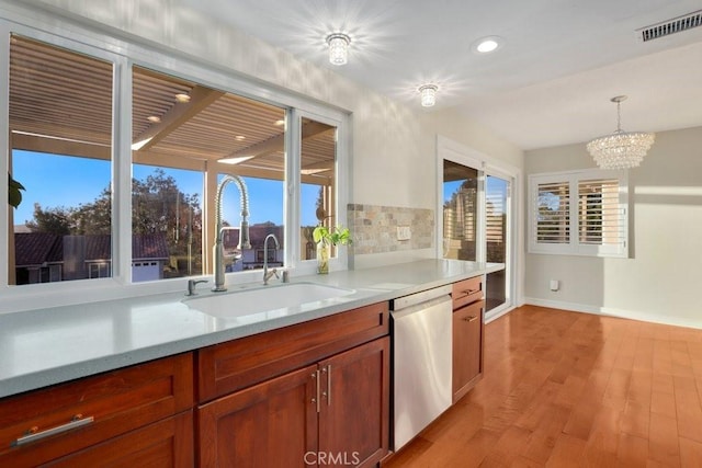 kitchen featuring pendant lighting, dishwasher, an inviting chandelier, light hardwood / wood-style floors, and sink