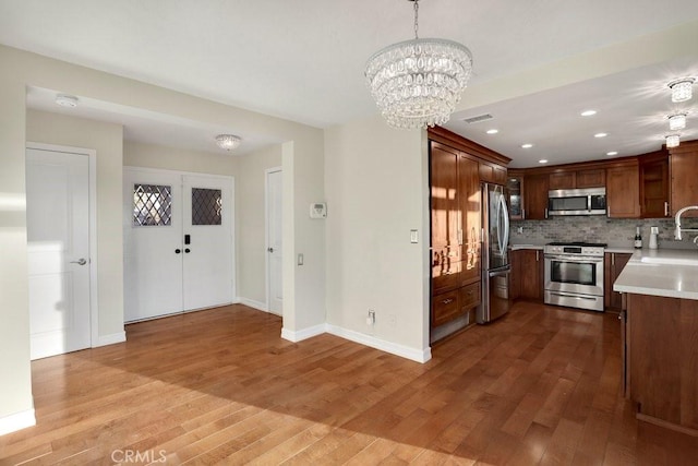 kitchen with pendant lighting, stainless steel appliances, decorative backsplash, sink, and light wood-type flooring