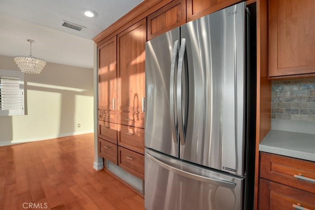 kitchen with backsplash, hanging light fixtures, stainless steel refrigerator, a chandelier, and light wood-type flooring