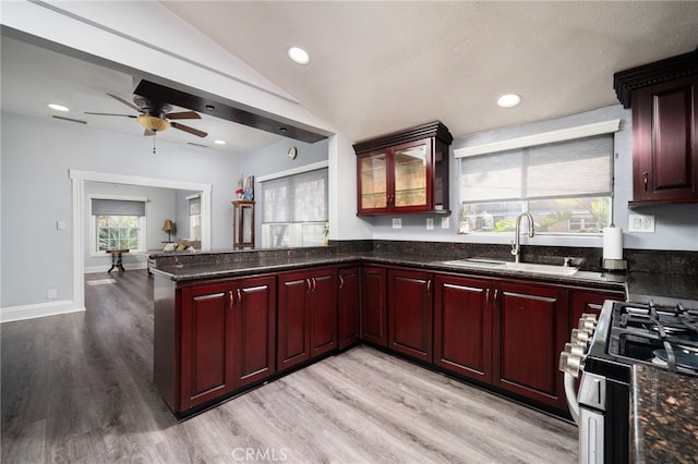 kitchen featuring kitchen peninsula, stainless steel gas range oven, light wood-type flooring, vaulted ceiling, and sink