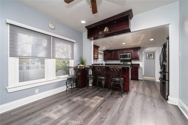 kitchen with ceiling fan, kitchen peninsula, dark wood-type flooring, a kitchen breakfast bar, and stainless steel appliances