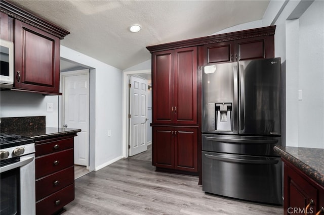 kitchen featuring appliances with stainless steel finishes, a textured ceiling, dark stone countertops, vaulted ceiling, and light hardwood / wood-style flooring