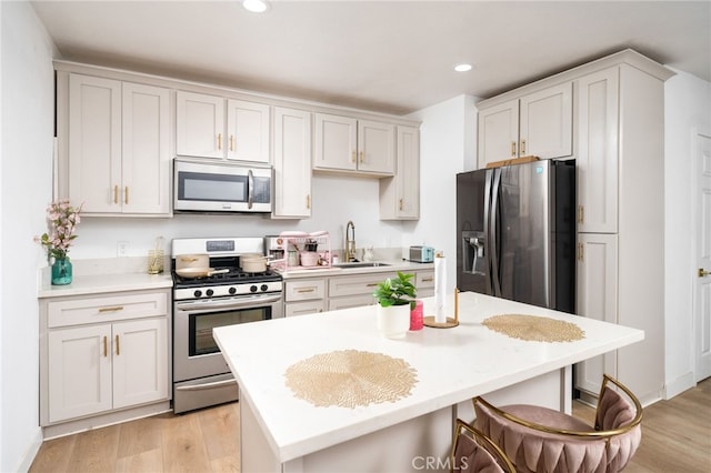 kitchen with a kitchen bar, sink, light hardwood / wood-style flooring, stainless steel appliances, and white cabinets