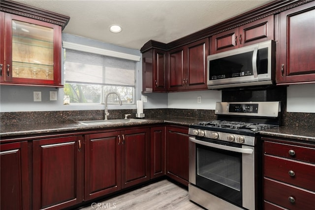 kitchen featuring light wood-type flooring, stainless steel appliances, dark stone countertops, and sink