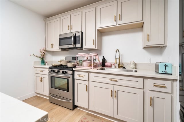 kitchen with stainless steel appliances, white cabinets, light hardwood / wood-style flooring, and sink