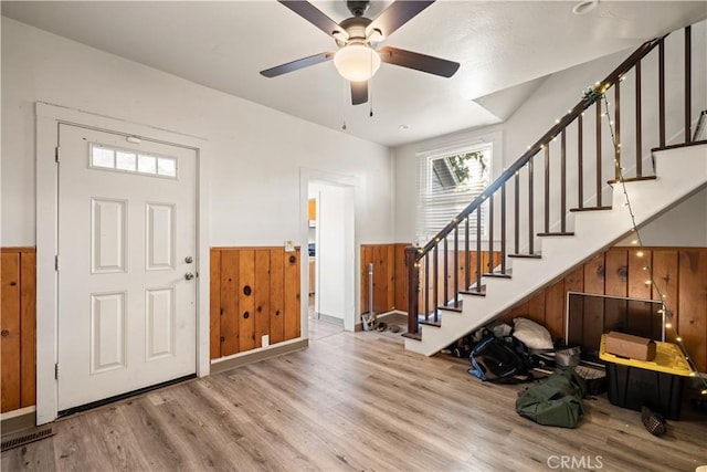 entrance foyer with ceiling fan, light hardwood / wood-style floors, and wooden walls