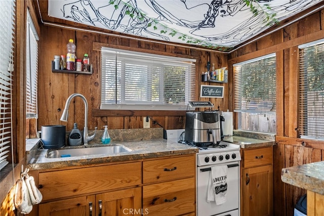 kitchen with dark stone countertops, sink, wood walls, and white gas range