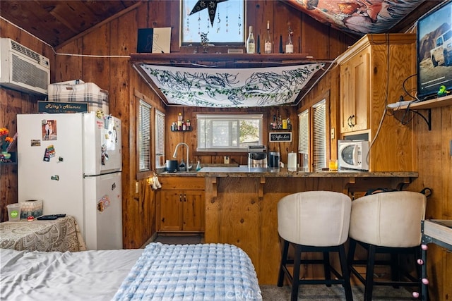 kitchen featuring an AC wall unit, lofted ceiling, white fridge, wooden walls, and sink