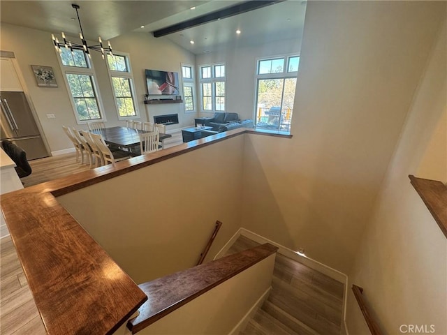 stairs with hardwood / wood-style floors, lofted ceiling with beams, and an inviting chandelier