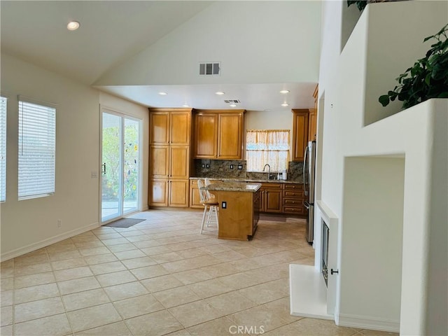 kitchen with stone countertops, stainless steel refrigerator, sink, a kitchen breakfast bar, and a center island