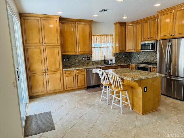 kitchen featuring a kitchen island, a breakfast bar area, decorative backsplash, light stone counters, and stainless steel appliances