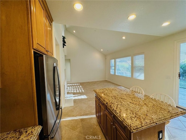 kitchen with lofted ceiling, a kitchen bar, stainless steel refrigerator, a kitchen island, and light stone countertops