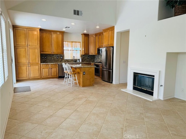 kitchen featuring a kitchen bar, tasteful backsplash, dark stone countertops, appliances with stainless steel finishes, and a kitchen island