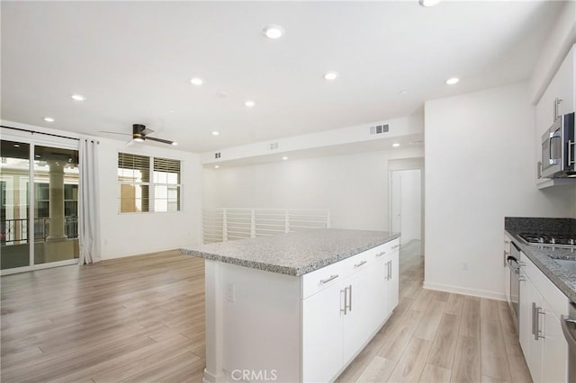 kitchen featuring ceiling fan, appliances with stainless steel finishes, white cabinetry, a center island, and light hardwood / wood-style floors