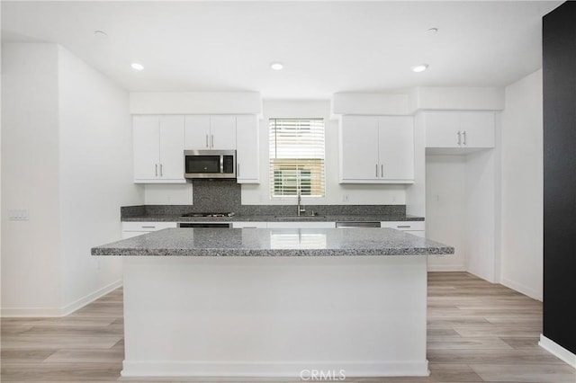 kitchen with white cabinetry, stainless steel appliances, dark stone counters, and a kitchen island