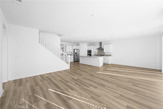 unfurnished living room with stairway, recessed lighting, and light wood-style flooring