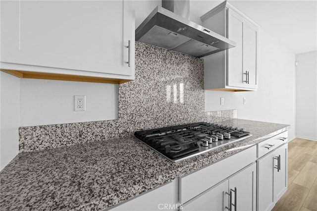 kitchen with light hardwood / wood-style flooring, wall chimney exhaust hood, white cabinets, dark stone countertops, and stainless steel gas cooktop