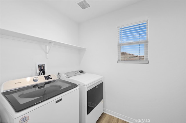 washroom featuring laundry area, light wood finished floors, visible vents, baseboards, and separate washer and dryer