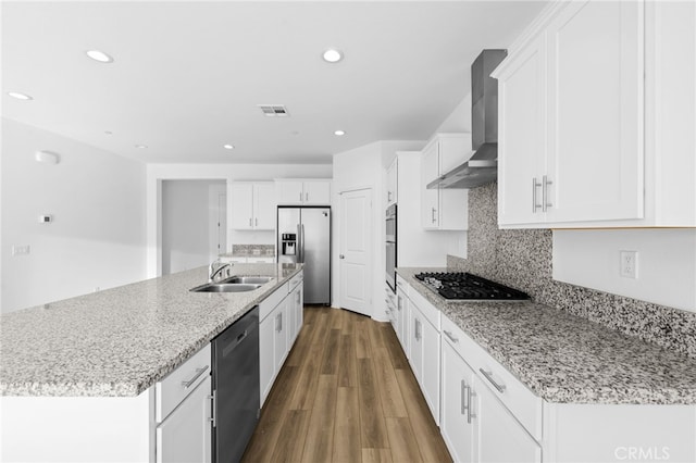 kitchen with dark wood finished floors, stainless steel appliances, white cabinetry, a sink, and wall chimney exhaust hood