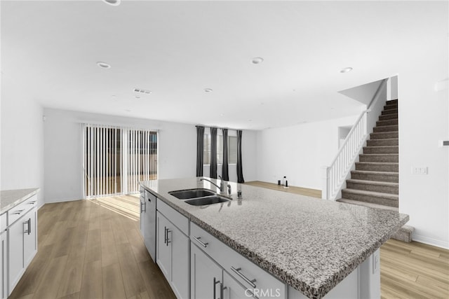 kitchen with sink, light wood-type flooring, a kitchen island with sink, and light stone countertops