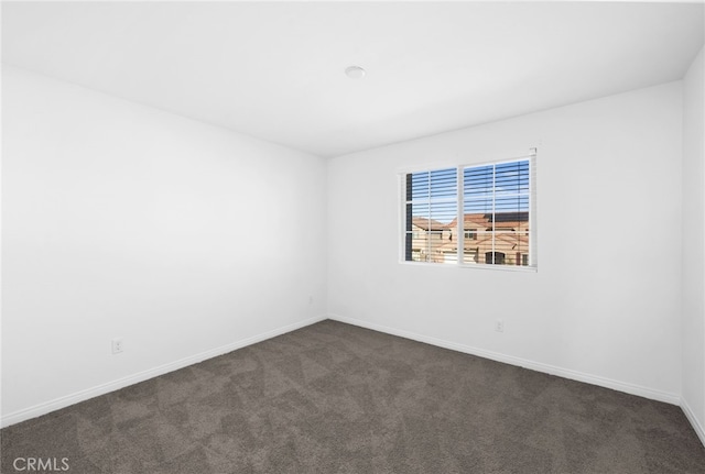 spare room featuring dark carpet and baseboards